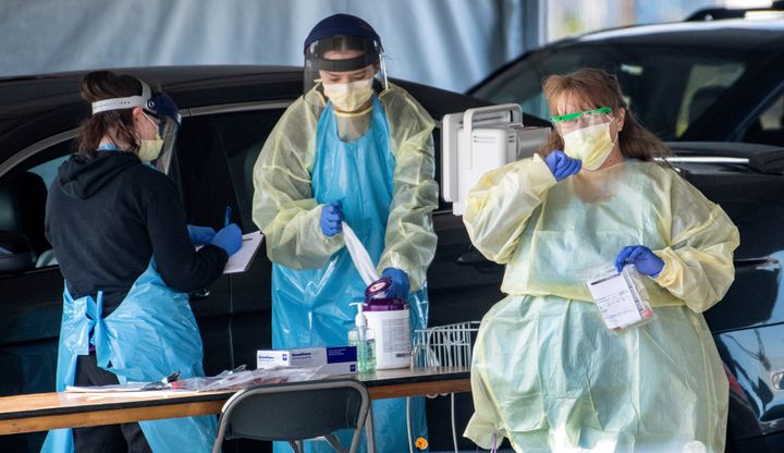 Medical personnel wearing protective equipment screen people referred by doctors for COVID-19 testing, Friday, March 20, 2020, at a drive-thru testing station set up in the parking lot at the Spokane County Fair & Expo Center in Spokane, Wash.