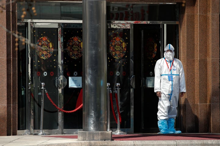 A worker wearing a protective suit stands outside a hotel converted into a quarantine location for travelers from overseas in