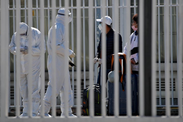 Workers in protective suits lead travelers to their transport outside the new China International Exhibition Center converted into a transit center for screening overseas arrivals in Beijing, on Tuesday, March 17, 2020. 