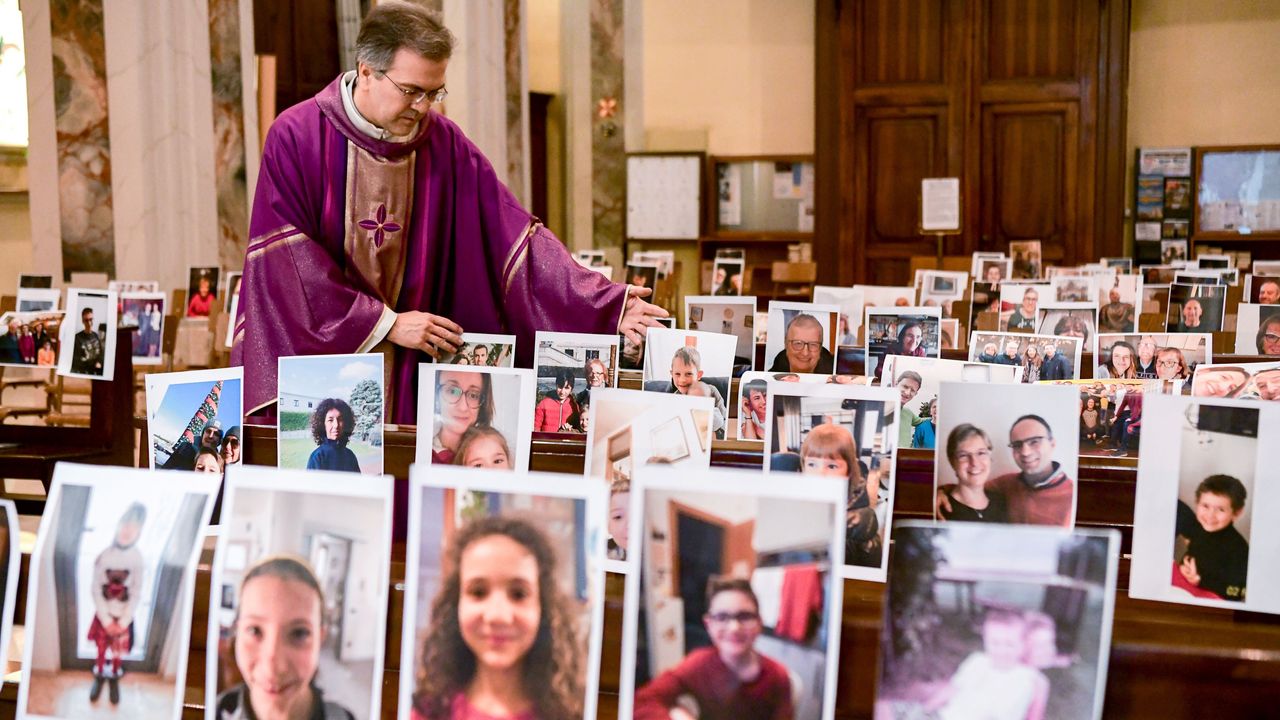 Don Giuseppe Corbari, parson of the Church of Robbiano, adjusts photos of his congregation at empty pews before celebrating Sunday Mass in Giussano, Italy, on March 22, 2020. 