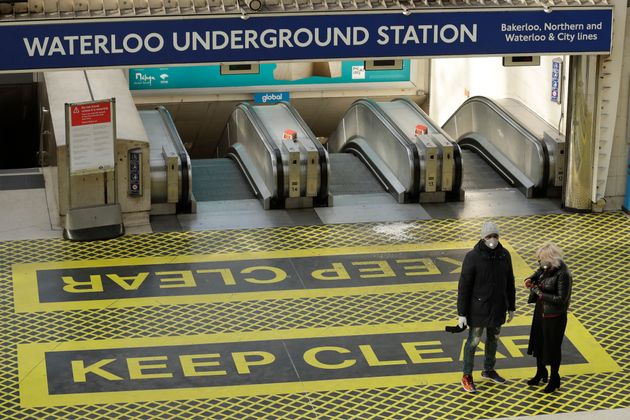 Two people waring masks stand at the top of a bank of escalators in London's Waterloo Station in London on Tuesday.