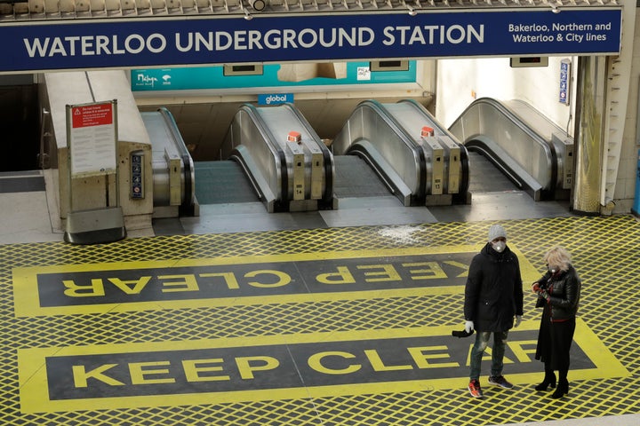 <strong>Two people waring masks stand at the top of a bank of escalators in London's Waterloo Station in London on Tuesday.</strong>