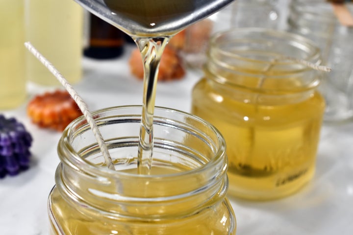 A close up image of pouring melted candle wax into glass molds.