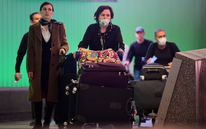 International travelers, some wearing face masks, arrive at Los Angeles International Airport on March 12, 2020, one day before a U.S. flight travel ban hit 26 European countries over the coronavirus.