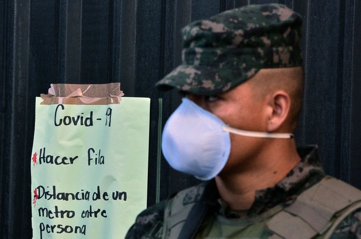 A soldier wearing a face mask stands next to a sign about preventive measures to stop the spread of COVID-19 in Honduras. The government declared a national curfew on March 16, 2020.