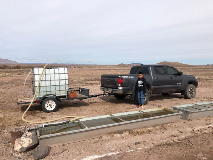Shanna Yazzie's 10-year-old son stands by the family's truck as water for their use is pumped from a nearby windmill.