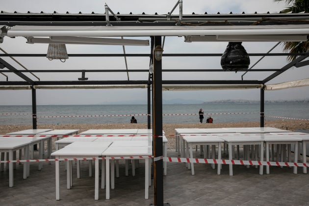 People relax on a beach behind a closed tavern at Alimos suburb of Athens, Sunday, March 22, 2020. Schools, restaurants, and other public places are already closed in the Greek capital aimed at slowing the spread of the new coronavirus, but other places like supermarkets, pharmacies and gas stations remain open. The COVID-19 illness causes mild or moderate symptoms in most people, but severe symptoms are more likely in the elderly or those with existing health problems. (AP Photo/Yorgos Karahalis)