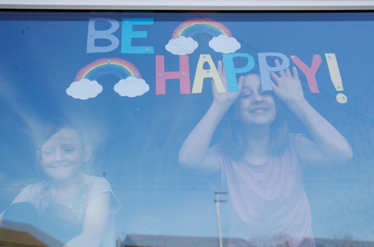 Η Σόφι και η Έμιλι Γουάρντ στέκονται μπροστά στο παράθυρο του σπιτιού τους, χαμογελούν ενώ στέλνουν το δικό τους μήνυμα με τον κορονοϊό να εξαπλώνεται στην περιοχή του Σεντ Χέλενς, στο Μέρσεϊσάιντ της Αγγλίας, την Τετάρτη, 25 Μαρτίου, 2020.