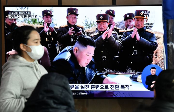 A woman wearing a face mask walks past a television news screen showing a file image of North Korean leader Kim Jong Un, at a railway station in Seoul on March 21, 2020. - North Korea on March 21 fired two projectiles presumed to be short-range ballistic missiles into the sea off its east coast, Seoul's military said. (Photo by Jung Yeon-je / AFP) (Photo by JUNG YEON-JE/AFP via Getty Images)