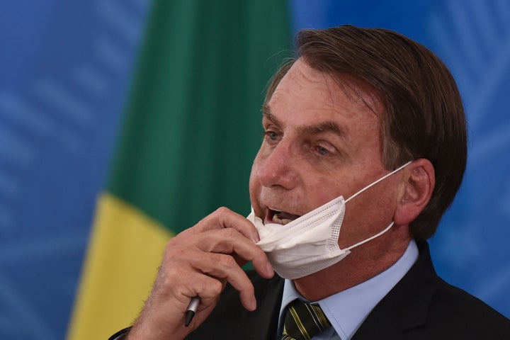 Brazil's President Jair Bolsonaro removes his mask to speak to journalists after a March 18 press conference on the new coronavirus at the Planalto Presidential Palace in Brasilia.