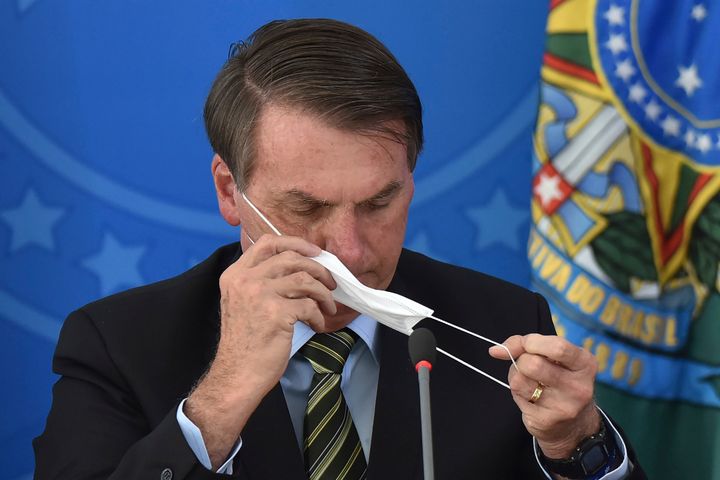 Brazil's President Jair Bolsonaro awkwardly puts on a mask during a March 18 press conference.