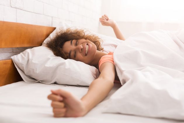 Happy woman waking up after sleep, lying in bed in the morning