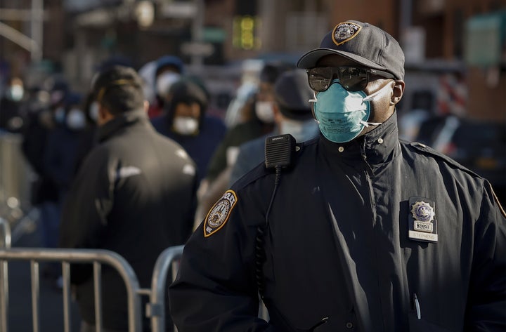 A New York City police officer wears protective gear while monitoring people waiting in line to be tested for the coronavirus