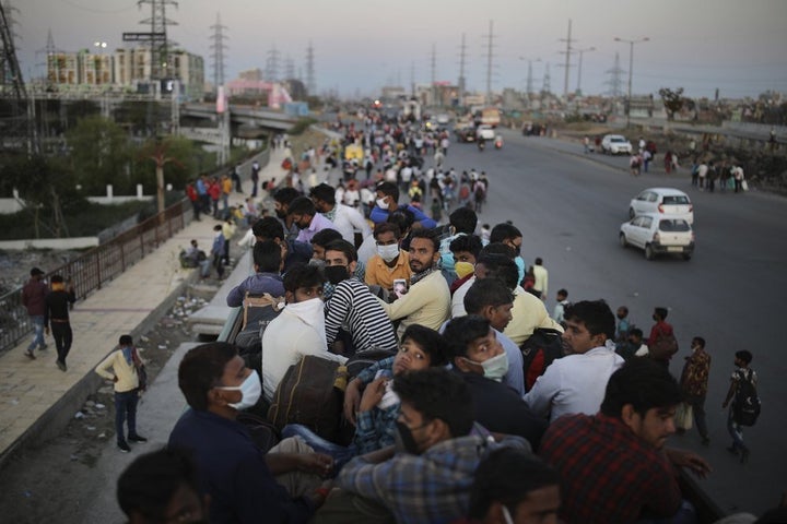 In this Saturday, March 28, 2020, photo, Indian migrant workers sit atop a bus, provided by the government, as others walk along an expressway to their villages.