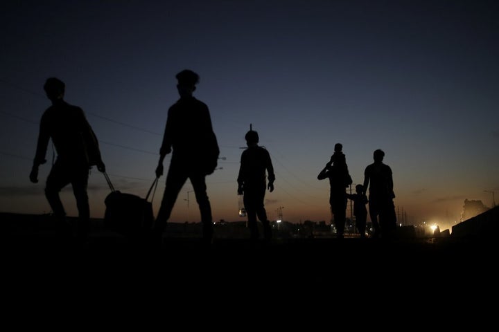 In this Saturday, March 28, 2020, photo, a migrant laborer's family is silhouetted as they proceed towards their village on foot from New Delhi, India.