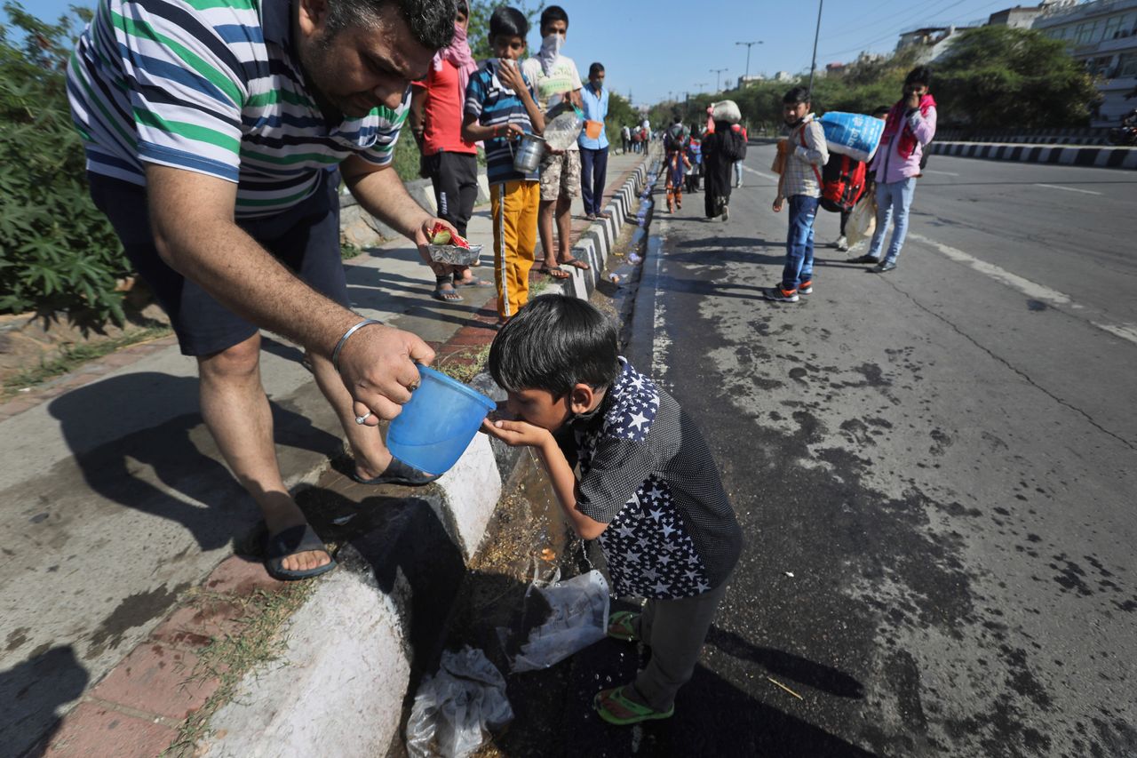 A man offers water to a child of a migrant daily wage labourer as he and his family make the journey on foot to their village following the imposition of the country's lockdown.