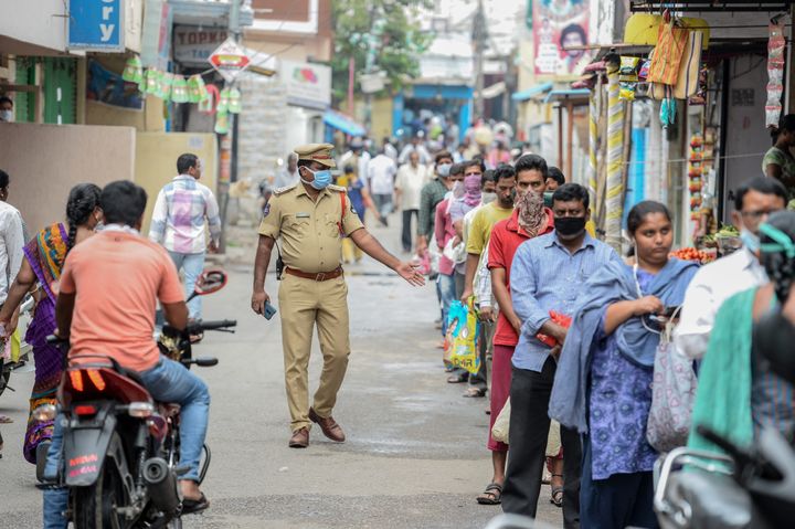A policeman patrols as people queue to receive free rice distributed at a government civil supply store, in Hyderabad on April 1, 2020. 