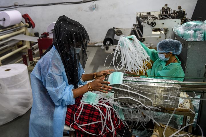 A worker collects facemasks from an assembly line at a facility of personal protective equipments manufacturer Nikshe Multiproducts on the outskirts of Ahmedabad on April 2, 2020. 