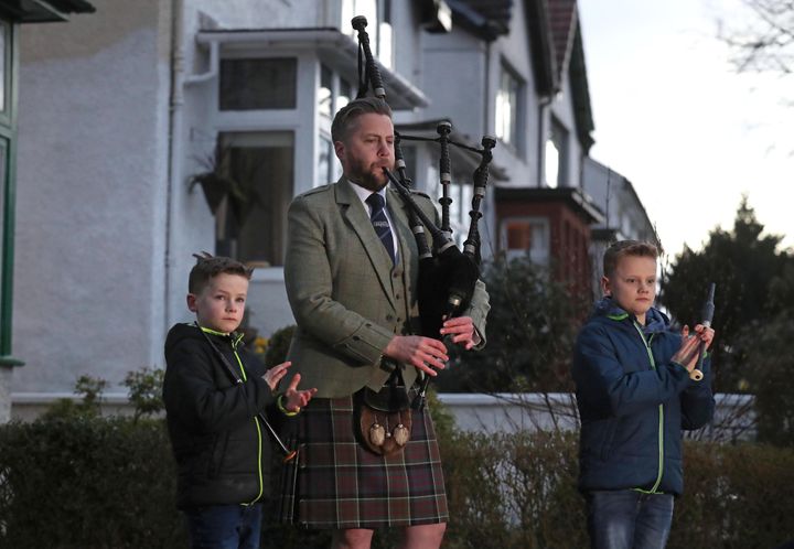 Finlay MacDonald plays the pipes at his home in Glasgow alongside sons Elliott, ten, and Fionn, eight, to salute local heroes.