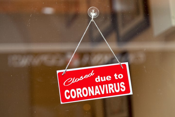 Red sign hanging at the glass door of a shop saying "Closed due to coronavirus".