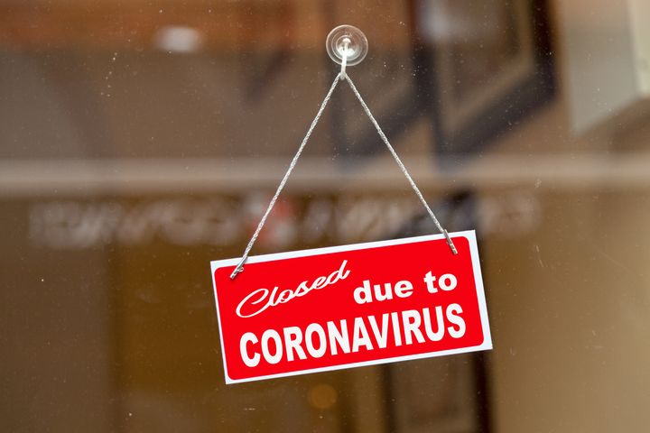 Red sign hanging at the glass door of a shop saying "Closed due to coronavirus".