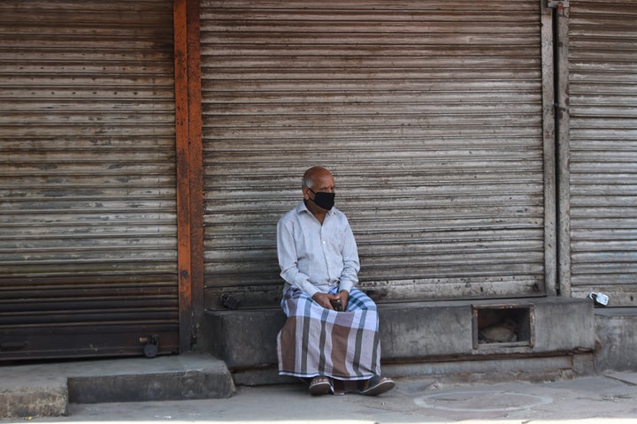 A man wearing a facemask sits outside closed shops during a government-imposed nationwide lockdown as a preventative measure against the COVID-19 novel coronavirus in the old quarters of New Delhi on March 30, 2020.