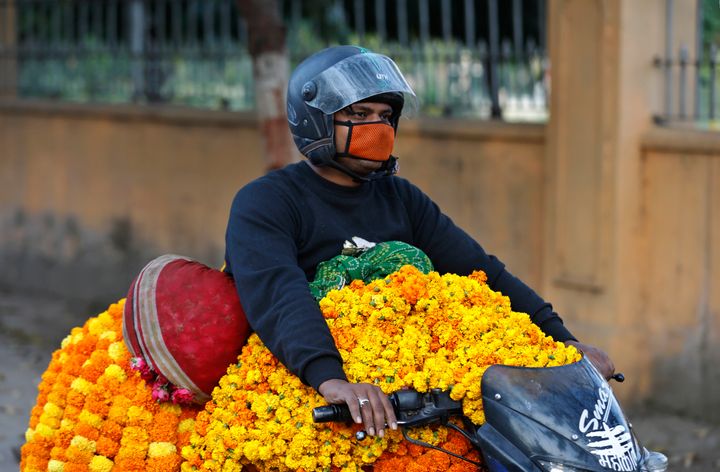 A man wearing a mask transports marigold flower garlands on a motorcycle during Navratri festival in Prayagraj, April 1, 2020.