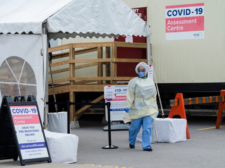 A health care worker wearing protective gear walks between a COVID-19 assessment centre at The Scarborough Hospital in Scarborough, Ont., on Friday.