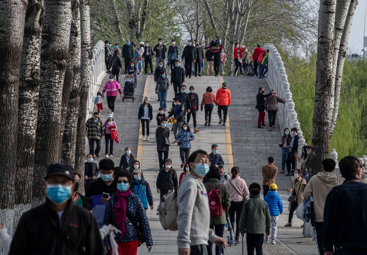 People wear protective masks as they walk while enjoying the spring weather at a park in Beijing, China.