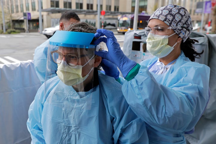 An emergency services nurse at Harborview Medical Center in Seattle helps a colleague put on a medical face shield prior to their shift in a triage tent used for arriving patients who have respiratory symptoms.