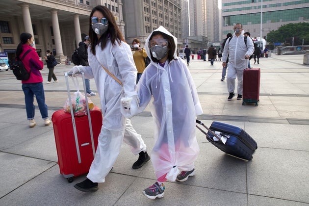 Passengers wearing face masks and raincoats to protect against the spread of new coronavirus walk outside...