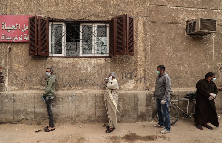 Men wearing masks wait outside an Egyptian Food Bank centre in Cairo to receive cartons with foodstuffs as the charity distributes aid to people who lost their jobs due to the coronavirus pandemic.