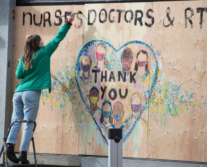 A woman paints a thank you message to nurses and doctors on a boarded up shop in downtown Vancouver on April 1, 2020. 