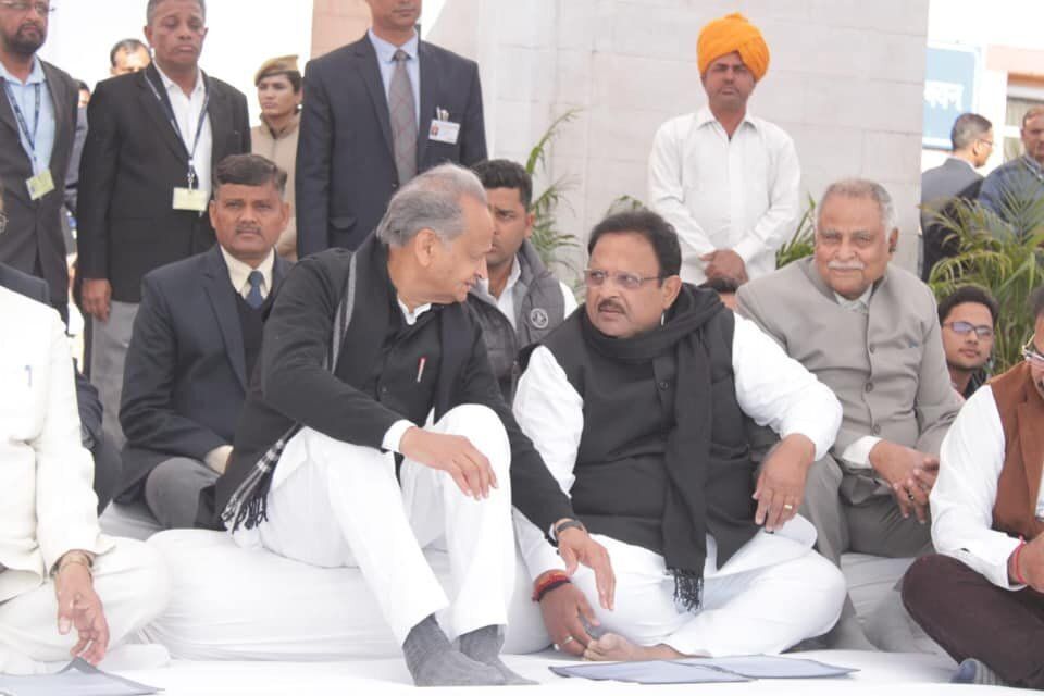 Rajasthan Health Minister Dr. Raghu Sharma (second from right; black shawl around neck) speaks with Chief Minister Ashok Gehlot at a public event. 