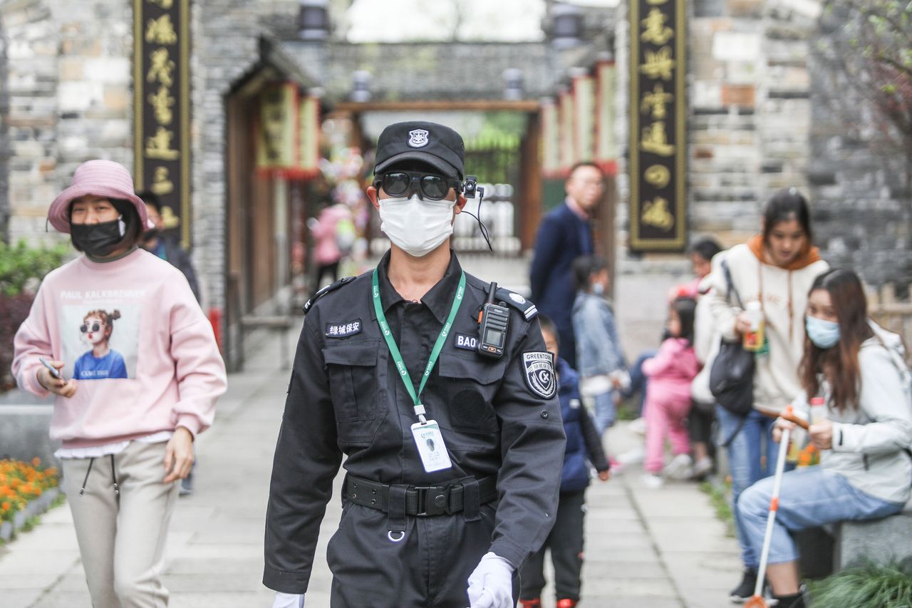 A security guard wearing augmented reality eyewear equipped with an infrared temperature detector walks by tourists in Hangzhou in east China's Zhejiang province