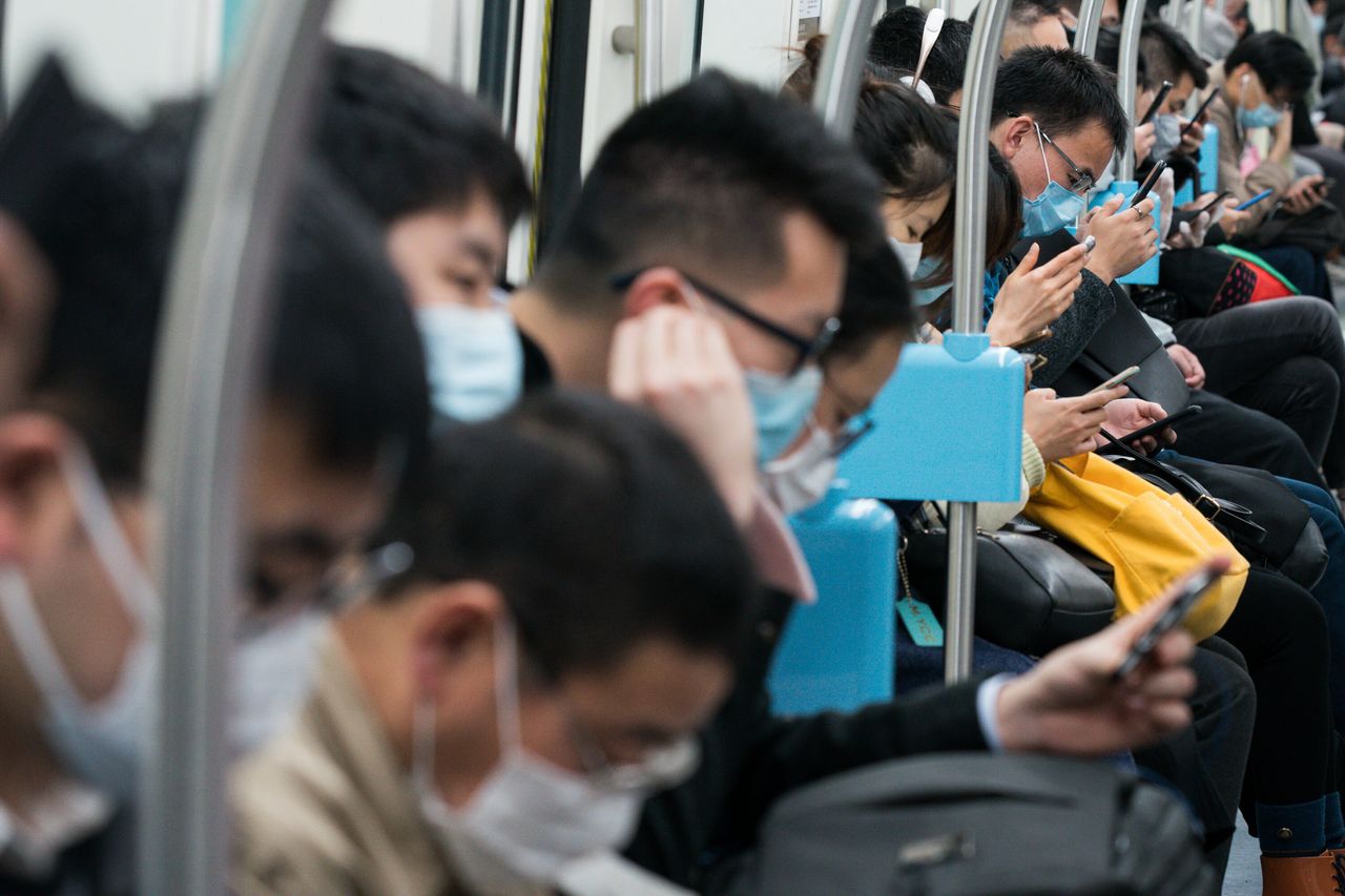 Commuters in protective masks look at their smartphones while riding a subway train in Shanghai