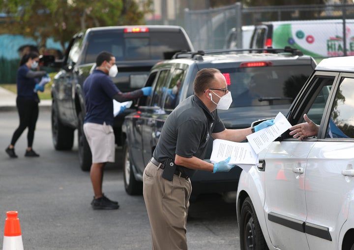 Eddie Rodriguez (right) and other Hialeah city employees hand out unemployment applications to people in their vehicles in front of the John F. Kennedy Library on April 8.