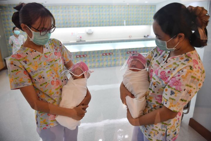 Nurses holding newborn babies wearing face shields at Bangkok's Praram 9 Hospital.