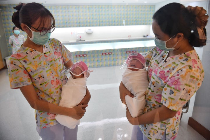 Nurses holding newborn babies wearing face shields at Bangkok's Praram 9 Hospital.