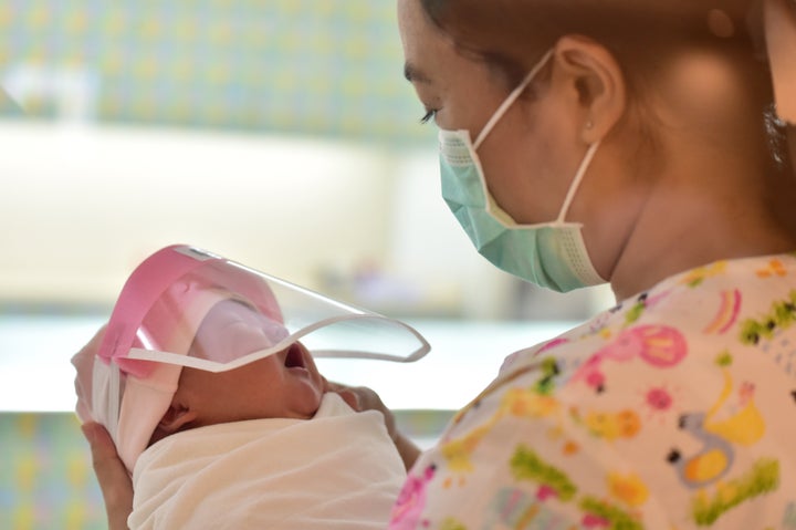 A nurse holding a newborn baby wearing a face shield — perhaps not happily — at Praram 9 Hospital.