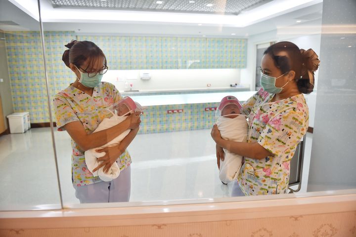 毛布に包まれた新生児が、医療用のマスクをした看護師たちに抱かれている。新生児や看護師たちの写真は、ガラス越しに撮影された。