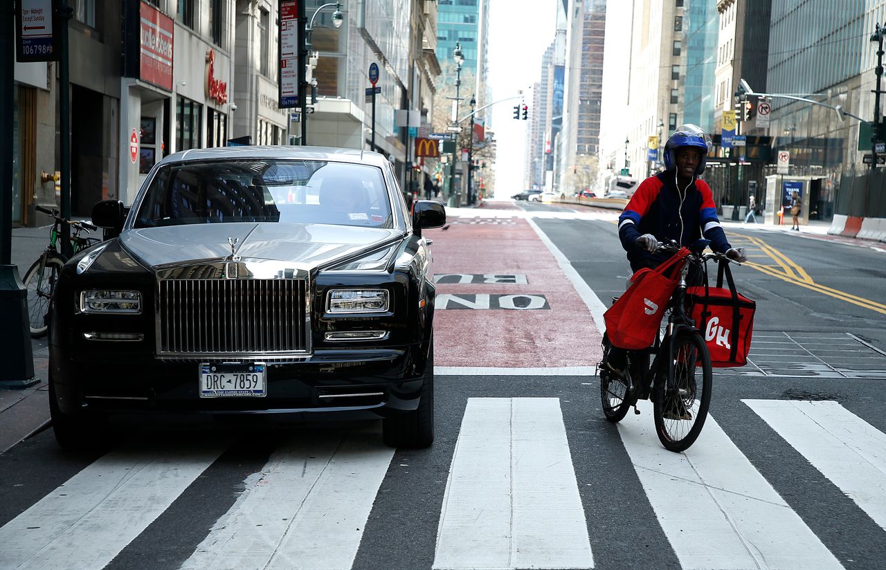 A delivery worker rides past a Rolls Royce amid the coronavirus pandemic on April 5, 2020 in New York City.