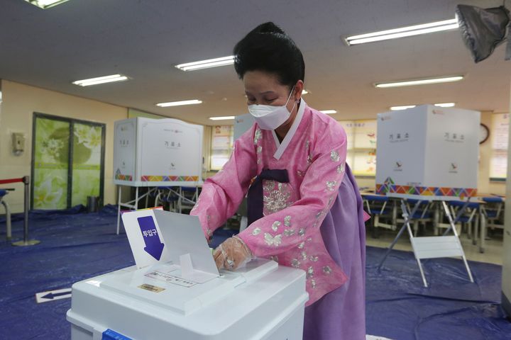 A woman wearing a face mask to help protect against the spread of the new coronavirus casts a vote for the parliamentary elections at a polling station in Seoul, South Korea, Wednesday, April 15, 2020. South Korean voters wore masks and moved slowly between lines of tape at polling stations on Wednesday to elect lawmakers in the shadows of the spreading coronavirus. (AP Photo/Ahn Young-joon)