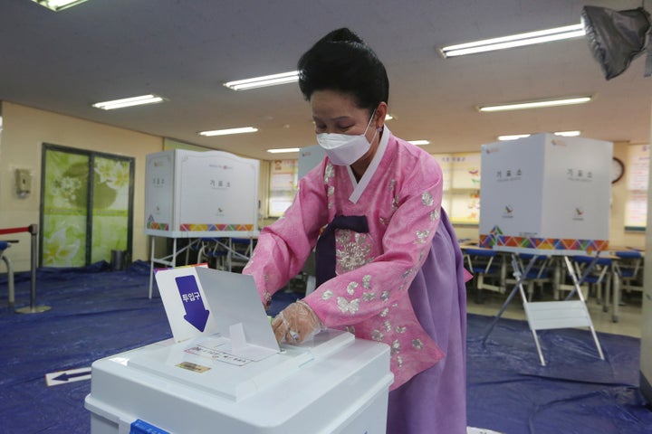 A woman wearing a face mask to help protect against the spread of the new coronavirus casts a vote for the parliamentary elections at a polling station in Seoul, South Korea, Wednesday, April 15, 2020. South Korean voters wore masks and moved slowly between lines of tape at polling stations on Wednesday to elect lawmakers in the shadows of the spreading coronavirus. (AP Photo/Ahn Young-joon)