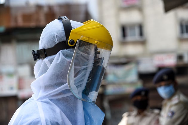 A health worker wearing protective gear walks past police personnel (background) during a screening and...