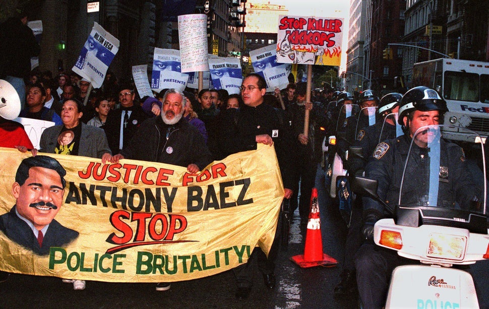 <em>Iris, left, and Ramon Baez, second from left, the parents of Anthony Baez, carry a banner as they march with at least 3