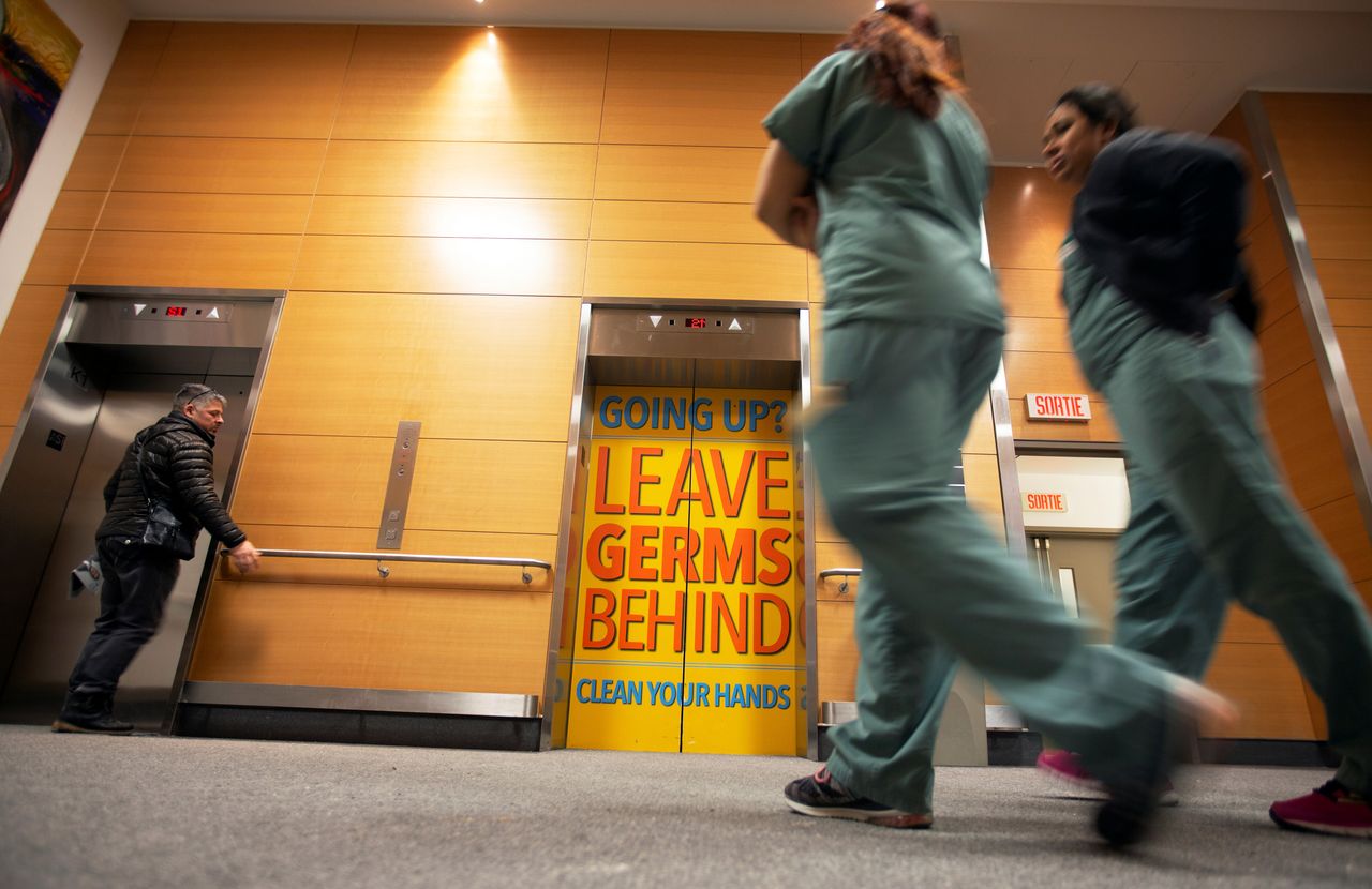 Staff and visitors walk past a sign indicating to wash hands on the elevator doors at the Jewish General Hospital in Montreal on March 2, 2020. 
