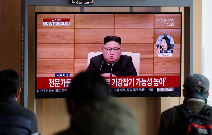 People watch a TV screen showing a news program reporting about North Korea's firing projectiles with a file footage of North
