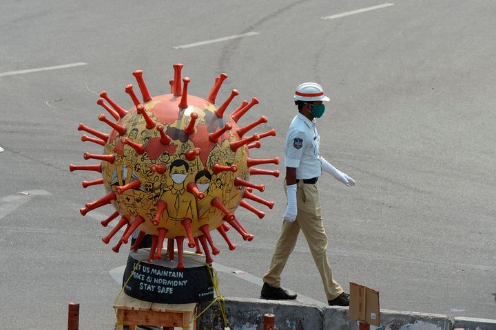 A traffic officer walks past a coronavirus-themed globe at a traffic junction in Hyderabad, on April 18, 2020.