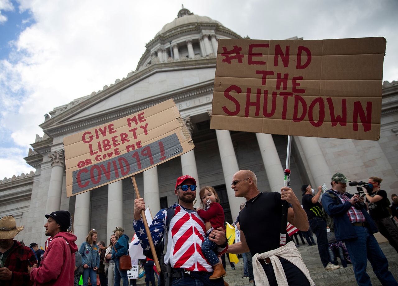 Two men hold signs as they protest against the state's extended stay-at-home order as hundreds gather to demonstrate at the Capitol building in Olympia, Washington.